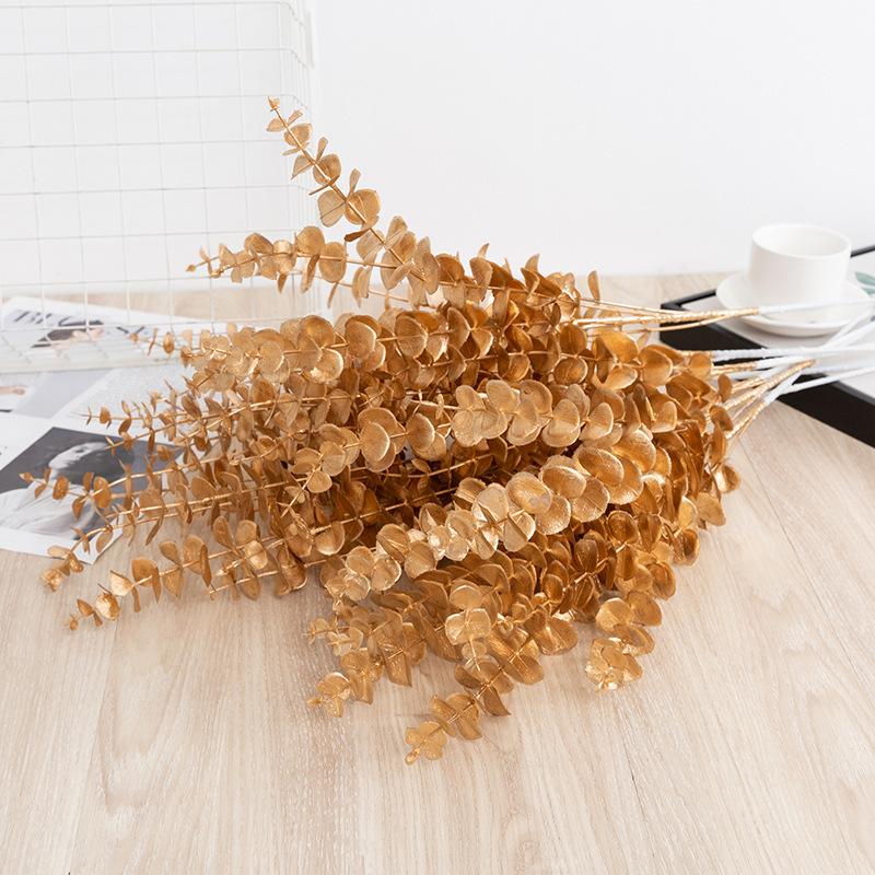 Trang trí đám cưới giả màu vàng: lá eucalyptus, hoa giả, cành giả, chi tiết vàng cho trang trí lối đi.