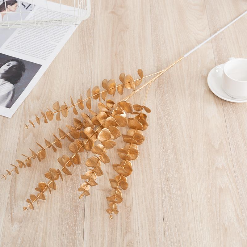 Trang trí đám cưới giả màu vàng: lá eucalyptus, hoa giả, cành giả, chi tiết vàng cho trang trí lối đi.